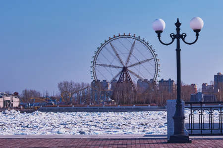 State border. The Amur river during the ice drift. View from the embankment of the city of Blagoveshchensk, Russia to the amusement park of the city of Heihe, China. Lantern, fencing and ferris wheel.の写真素材