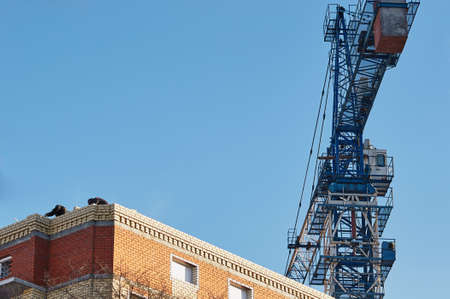 Construction of a brick house. Construction crane. Builders are laying bricks. Early morning.