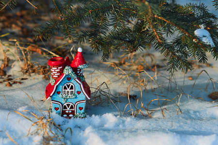 A toy house in the snow under the spruce branches.の写真素材