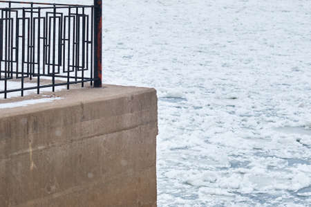 Black metal fence of the city embankment. Spring river Amur during ice drift in blur in the background.の写真素材
