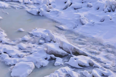 Pieces of ice covered with white snow on a frozen river. Winter background texture. Highlights and...