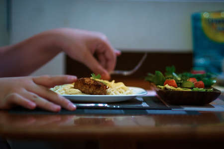 Side view while eating. Hands over a dish with pasta and cutlet. Vegetable salad. Selective focus.