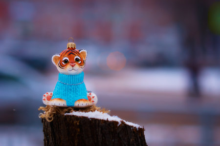 Tiger cub in a blue sweater on a stump in winter. Toy for the Christmas tree. Snowing. City street with transport in strong blur. Tiger is the symbol of 2022 on the Chinese calendar. Selective focus.の写真素材