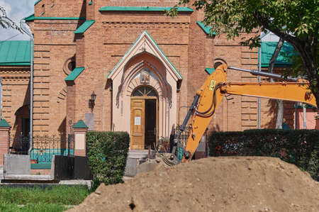 Christian church. The excavator conducts road works against the backdrop of the building of the temple. Russian Orthodox Church. The building is in the Catholic style.の写真素材