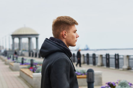 A serious blond man in a leather jacket stands on the city embankment against the backdrop of a rotunda. Side view. Blur the background. Blagoveshchensk, Russia.の写真素材