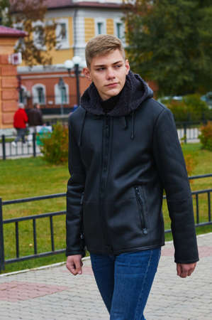A young guy walks down the street in a warm jacket with a hood and jeans. Early autumn. Selective focus. Blagoveshchensk, Russia.の写真素材