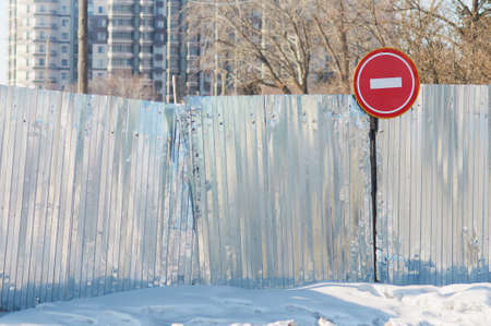 Road sign No Entry on a metal fence. Road closed red round sign. White brick in a red circle road sign. Sunny winter day. closed construction site.の写真素材