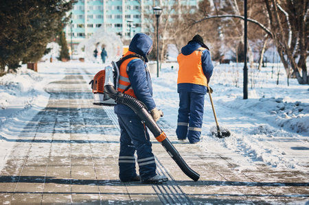 City utility workers in bright orange suits clear snow from city streets. Clearing the footpath from...