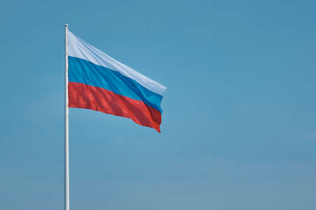 Flag of Russia against the blue sky. High flagpole on the embankment of the city of Blagoveshchensk, Russia. The tricolor cloth moves smoothly in the wind. Room for text.の写真素材