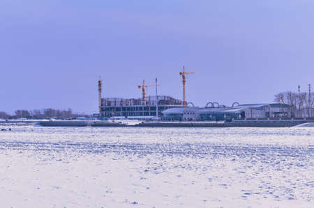 View of the construction of the Chinese terminal of the international cable car from the Russian bank of the Amur River. February 2022. Snow and border barriers on ice. Blue purple morning sky.の写真素材