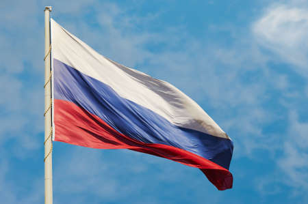 The national flag of the Russian Federation flutters in the wind against a blue sky with white clouds. The tricolor symbol of the state, attached to a pole with a cord. bright sunny day.の写真素材