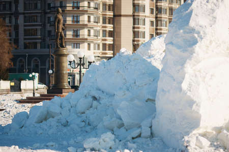 A pile of frozen chunks of snow on the sidewalk. Destroyed New Year's ice slide. The monument and residential building are blurred in the background. Sunny winter day. selective focus.の写真素材