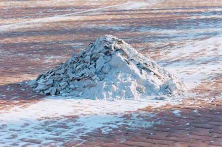 Snow removal in the city. Snow pile on the sidewalk in the form of a volcano. The work of urban services in the winter. Red paving slabs. Long evening shadows. Volcano.の写真素材