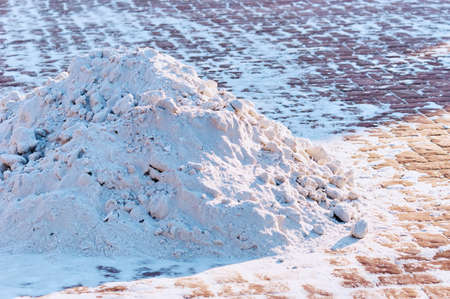 Snow removal in the city. Snow pile on the sidewalk in the form of a volcano. The work of urban services in the winter. Red paving slabs. Long evening shadows. Volcano.の写真素材