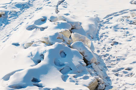 Deep crack on the snow-covered ice of the Amur River on a sunny day. footprints. Fracture of the ice surface in winter. The concept of destruction and overcoming obstacles. Dangerous cracked iceの写真素材