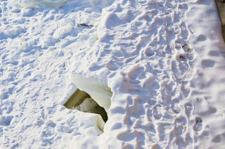 Deep crack on the snow-covered ice of the Amur River on a sunny day. footprints. Fracture of the ice surface in winter. The concept of destruction and overcoming obstacles. Dangerous cracked iceの写真素材