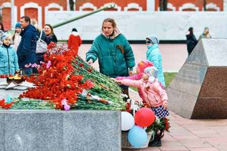 BLAGOVESHCHENSK, RUSSIA - MAY 9, 2021: Laying flowers at the monument - the symbol of May 9, the memory of the war. girls with carnations. St. George's ribbon on clothes.のeditorial素材
