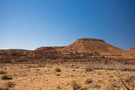 Old village hidden on the desert valley between hills on blue sky backgroundの写真素材