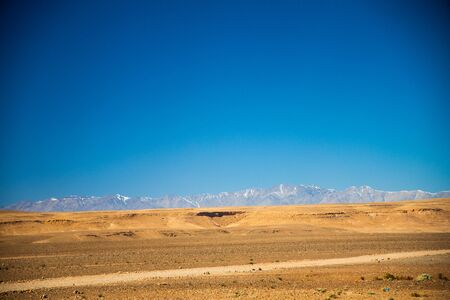 Desert road lies among the valley with Atlas mountains and blue sky backgroundの写真素材
