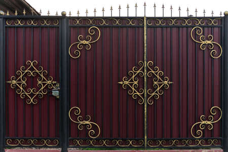 Ornate and beautiful wrought iron fence gate painted scarlet brown and gold. A photo of a natural old gate for use as a texture.の写真素材