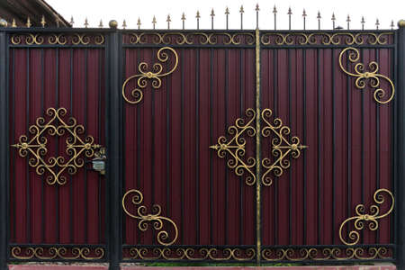 Ornate and beautiful wrought iron fence gate painted scarlet brown and gold. A photo of a natural old gate for use as a texture.