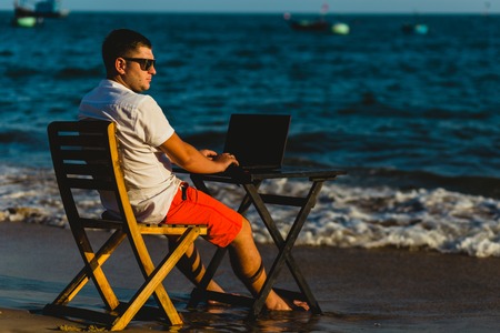 Man working with a laptop, on a hammock in the beach. Concept of digital nomad, remote worker, independent location entrepreneur.の写真素材