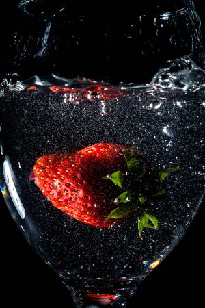Strawberries splashing into water on a black backgroundの写真素材