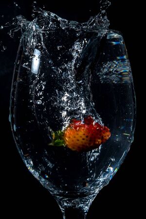 Strawberries splashing into water on a black backgroundの写真素材