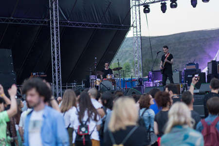 Audience with hands raised at a music festival and lights streaming down from above the stage. Soft...
