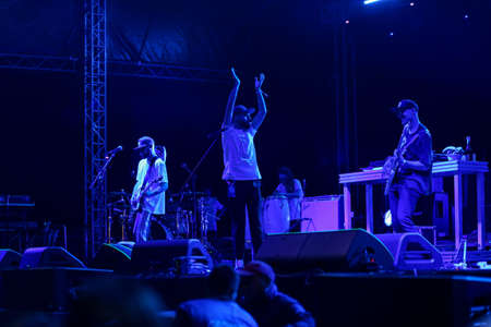 Audience with hands raised at a music festival and lights streaming down from above the stage. Soft...