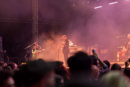 Audience with hands raised at a music festival and lights streaming down from above the stage. Soft focus, high ISO, grainy image.のeditorial素材