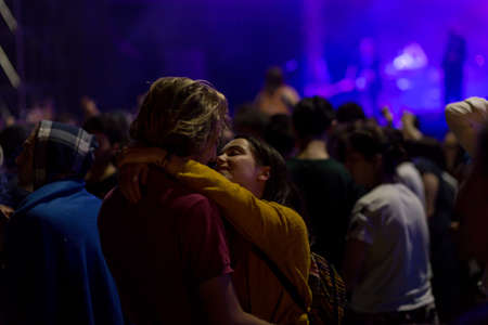 Audience with hands raised at a music festival and lights streaming down from above the stage. Soft...