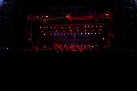 Audience with hands raised at a music festival and lights streaming down from above the stage. Soft...