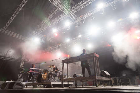 Audience with hands raised at a music festival and lights streaming down from above the stage. Soft focus, high ISO, grainy image.のeditorial素材