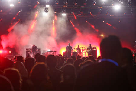 Audience with hands raised at a music festival and lights streaming down from above the stage. Soft focus, high ISO, grainy image.のeditorial素材