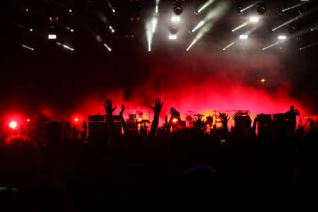Audience with hands raised at a music festival and lights streaming down from above the stage. Soft focus, high ISO, grainy image.のeditorial素材