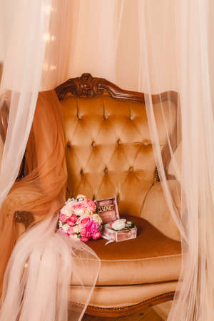 A beautiful wedding bouquet of roses and peonies, and a box with flowers and rings on a leather armchair. Wedding day of the bride and groom. Blurred background.の写真素材