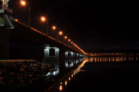Night view of the bridge over the Kola river. The city of Murmansk. A long bridge with illuminated lanterns reflecting in the water. Murmansk regionの写真素材