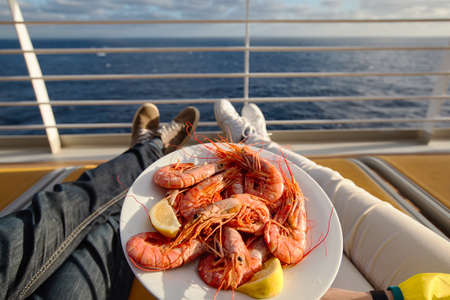 a young couple holds a plate with shrimps while on a cruise shipの写真素材