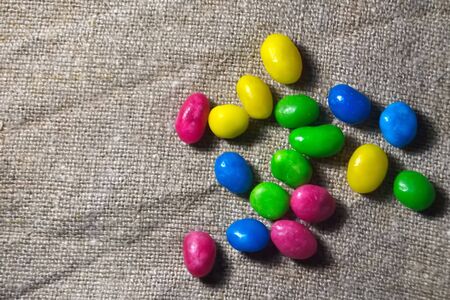 Multicolored round candy lying on the burlap. Multi-colored candies dragee. Small round candy