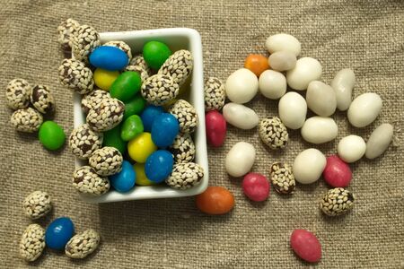 Multicolored round candy lying on the burlap. Multi-colored candies dragee. Small round candy