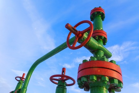 Horizontal view of a wellhead with valve armature. Oil and gas industry concept.  Oil valve with rocking in the background. Offshore oil and gas site service operator open valve for control gases.の写真素材