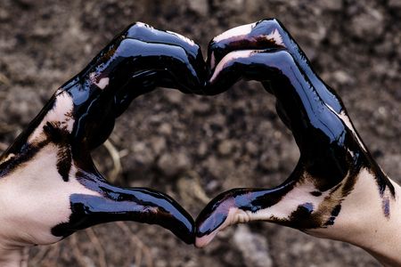 oil leaking. Very dirty hand.Stain hands showing thumbs up with black oil on soil background.の写真素材