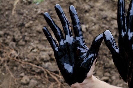 oil leaking. Very dirty hand.Stain hands showing thumbs up with black oil on soil background.の写真素材