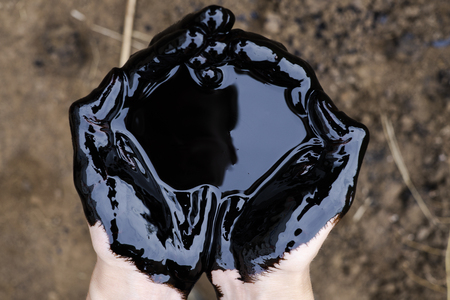 oil leaking. Very dirty hand.Stain hands showing thumbs up with black oil on soil background.の写真素材
