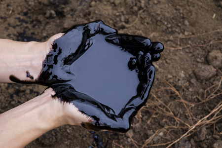oil leaking. Very dirty hand.Stain hands showing thumbs up with black oil on soil background.の写真素材
