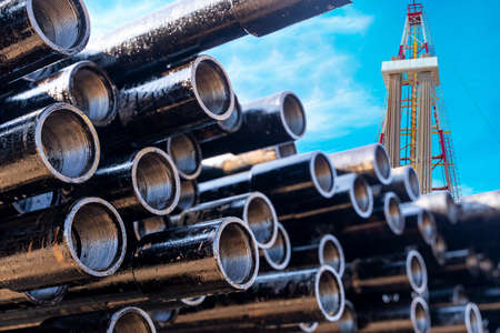 In the foreground pipes for drilling oil and gas wells. In the background, a blurred image of the rig out of focus. Blue sky with cloudsの写真素材