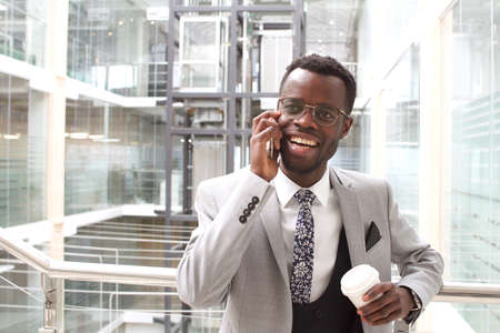 Smiling businessman in black suit talking on smartphone holding Cup of coffee in hands.の写真素材