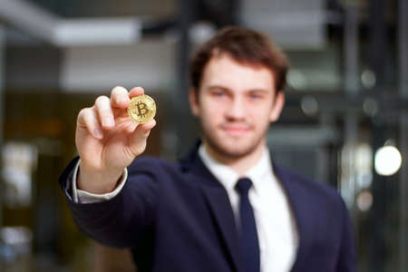 Golden Bitcoin in hand with businessman blurred on background, Digital symbol of new virtual...