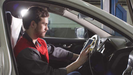 Mechanic sitting in car doing diagnostics on digital tablet
